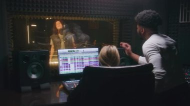 Deneyimli ses mühendisi ve Afrikalı Amerikalı yapımcı ses kayıt stüdyosunda şarkıcıyla çalışıyor. Bilgisayar ekranı müzik yaratmak için DAW yazılım arayüzünü gösterir. Müzik üretimi kavramı.
