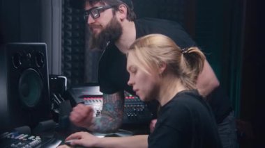 Kadın ses mühendisi karıştırma konsolu kullanır, ses kayıt stüdyosunda yapımcıyla yeni bir şarkı ya da DJ seti oluşturur. Bilgisayar ekranı DAW program arayüzünü ses parçalarıyla gösteriyor. Müzik üretim konsepti.