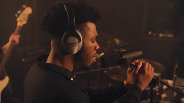 非洲裔美国歌手在隔音室内录制新歌的特写镜头 音乐家在背景音乐上演奏乐器 在录音室里听录音 音乐制作的概念 — 图库视频影像