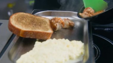 Erkek aşçı tavadan kızarmış karidesi kızarmış ekmek ve çırpılmış yumurtayla birlikte tabağa koyar. Şef lezzetli yemekler pişirir. Restoran mutfağında yemek pişirme süreci. Profesyonel gurme mutfağı. Kamu hizmeti.