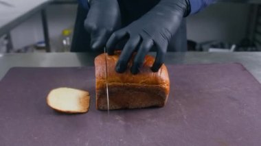 Eldiven giymiş bir erkek aşçı sandviç ya da tost için tahtayı bıçakla kesiyor. Şefin elleri yakın olsun. Yemek pişirme süreci. Profesyonel mutfağı olan restoran mutfağı. Kamu hizmeti.