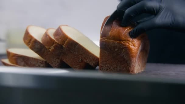 サンドイッチやトーストのためのまな板にナイフで新鮮な白いパンを切断手袋で調理のショットを閉じます 調理プロセス プロの料理とレストランキッチン 公共用ケータリング — ストック動画
