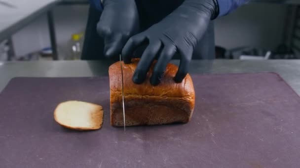 手袋の男性料理はサンドイッチやトーストのためのまな板にナイフで新鮮な白いパンをカットします シェフの手を閉じてください 調理プロセス プロの料理とレストランキッチン 公共用ケータリング — ストック動画