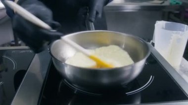 Erkek aşçı kızartma yapar ve çırpılmış yumurtaları indüksiyon sobasında kızartma tavasına karıştırır. Şef lezzetli kahvaltı yemekleri pişirir. Lokanta ya da kafe mutfağında aşçılık. Profesyonel mutfağa. Kamu hizmeti.