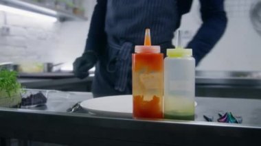 Erkek aşçı mutfakta bulaşık sunumu yapmaya hazırlanıyor. Aşçı masaya sos koyar ve mikroyeşillikleri küçük mutfak makasıyla kesmeye başlar. Profesyonel mutfağı olan bir restoran. Kamu hizmeti.