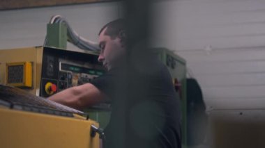 ZAPORIZHYA, UKRAINE - 25 Mart 2023: Erkek teknisyen CNC Bilgisayarlı Sayısal Kontrol kullanarak torna makinesi kurdu. Fabrikada sinema lensleri üretiliyor. Üretim, metalcilik ve