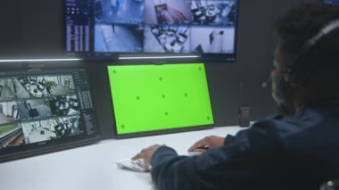 Afrikalı Amerikalı erkek operatör güvenlik kontrol merkezinde çalışıyor. Büyük dijital ekran ve güvenlik kameralı bilgisayar monitörleri. Arkaplanda tablet olan bir işçi. Yeşil Ekran.