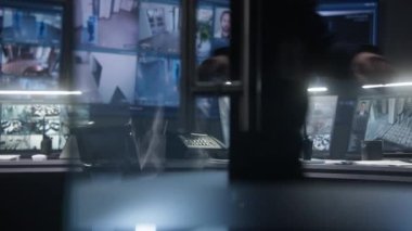 Kulaklık tipi klavyeli kadın operatör ve yapay zeka yüz taramasıyla güvenlik kameralarını kontrol ediyor. Bilgisayarlı monitörler ve duvardaki büyük dijital ekranlar CCTV kamera görüntülerini gösteriyor. Gözetim merkezinde çalış..