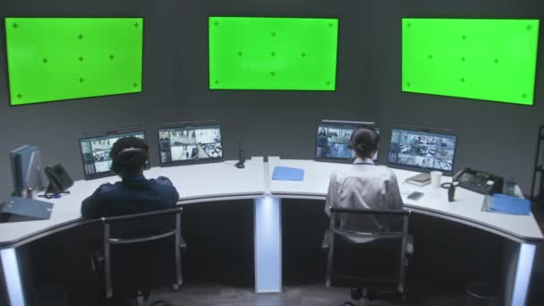 多民族の男性と女性の役員はCctvカメラを制御します 従業員はセキュリティコントロールセンターで働いています 監視カメラのビデオ映像を示すコンピュータモニタ クロマキー付きの大きなデジタルスクリーン — ストック動画