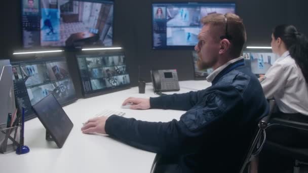 在警察监控中心 耳机中的男性安全操作员用人工智能面部识别来控制闭路电视摄像机 平板电脑 电脑显示器和显示安全摄像头镜头的大型数字屏幕 — 图库视频影像