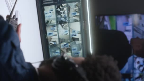 ヘッドセットのアフリカ系アメリカ人のセキュリティ担当者は 監視制御センターのCctvカメラを制御します 監視カメラのビデオ映像は コンピュータモニタと大きなデジタル画面に表示されます 垂直表示 — ストック動画