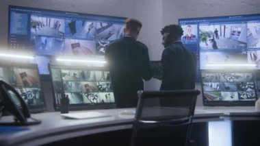Çok ırklı çalışanlar konuşuyor ve CCTV kameralarını kontrol ediyor. Yapay zeka da izleme merkezinde birlikte tarama yapıyor. Duvarda güvenlik kamerası görüntülerini gösteren büyük ekranlar var. Sosyal güvenlik kavramı.