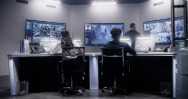 Güvenlik görevlilerinden oluşan çok ırklı bir ekip gözetim odasında çalışıyor. Duvarda güvenlik kamerası görüntüsü olan bir sürü büyük ekran var. İzleme ve izleme sistemleri. Sosyal güvenlik kavramı.