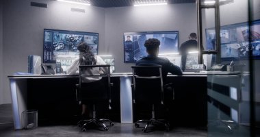 Güvenlik görevlilerinden oluşan çok ırklı bir ekip gözetim odasında çalışıyor. Duvarda güvenlik kamerası görüntüsü olan bir sürü büyük ekran var. İzleme ve izleme sistemleri. Sosyal güvenlik kavramı.