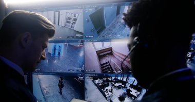 Çok ırklı çalışanlar, polis izleme merkezinde yapay zeka yüz tanıma sistemiyle mobese kameralarını kontrol ediyor. Duvardaki büyük ekran güvenlik kamerası görüntülerini gösteriyor. Sosyal güvenlik kavramı. Arkadan bak. Kapat..