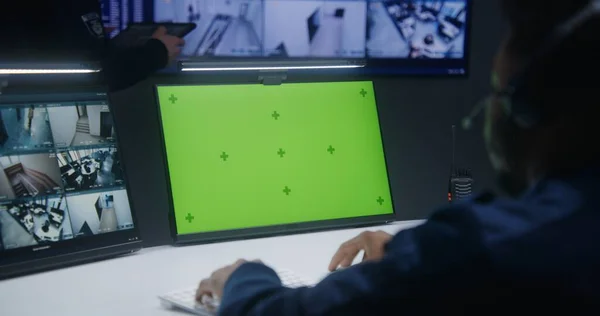 非裔美国男性官员控制着监控中心的闭路电视摄像头 带有色键的计算机监视器 背景上有监控摄像头视频镜头的工人和大数字屏幕 — 图库照片