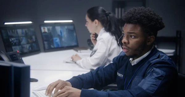 非裔美国人安全操作员在耳机类型的键盘和看监视器在警察监视室 女警官在背景下工作 显示闭路电视摄像头镜头的电脑屏幕 靠近点 — 图库照片