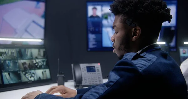 非裔美国官员控制闭路电视摄像头 人工智能面部扫描在警察监测室 女操作员在后台工作 墙上的大屏幕显示了摄像头的镜头 靠近点 — 图库照片