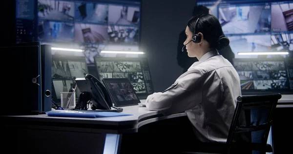 stock image Female security officer in headset zooms and controls CCTV cameras using tablet. Colleagues work at background. Multiple big screens on the wall showing CCTV footage. Monitoring. Social safety concept