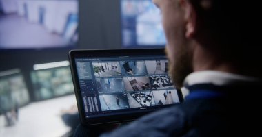 Güvenlik görevlisinin güvenlik kameralarını AI yüz taramasıyla yakınlaştırırken polis gözetleme merkezinde tablet kullanırken yakın plan görüntüsü. Meslektaşlar arka planda çalışır. İzleme sistemi. Sosyal güvenlik kavramı.