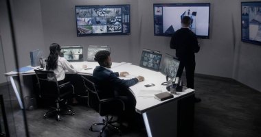 Çok ırklı güvenlik görevlileri güvenlik kameralarını yapay zeka ile tarıyor. Güvenlik kameraları olan bir sürü büyük ekran. Gözetleme odasında ekip çalışması. İzleme, izleme ve sosyal güvenlik.