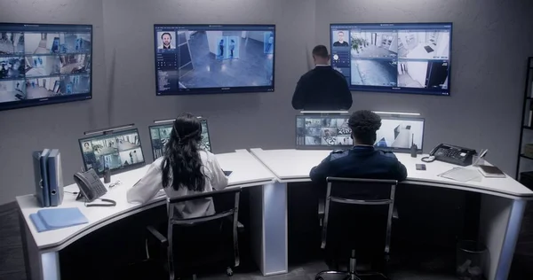 多族裔安全官员使用人工智能面部扫描对闭路电视摄像机进行监测 多个大屏幕与显示的安全摄像头 监视室的团队合作 跟踪和社会安全 — 图库照片
