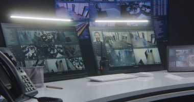 Bilgisayar monitörleri ve tablet yapay zeka yüz tanıma sistemi olan güvenlik kameralarının görüntülerini gösteriyor. Arka plandaki duvarda büyük dijital ekran var. Modern güvenlik kontrol merkezi. Zaman Uygulaması.