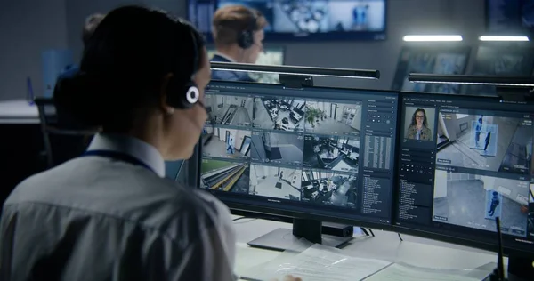 Diverse employees work in security control center, watch CCTV cameras with AI face scanning. Female operator uses PC. Computer monitors and big digital screens with surveillance cameras video footage.