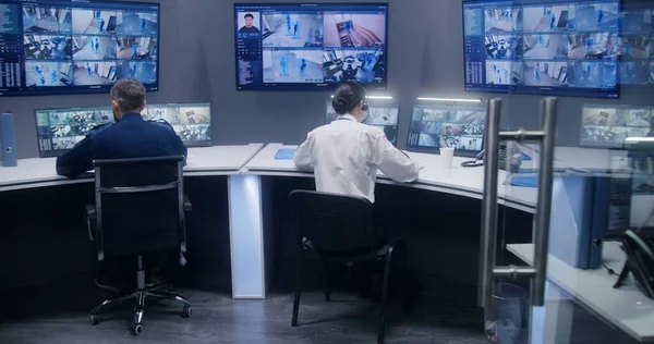 多样化的官员团队使用人工智能面部识别系统观看闭路电视摄像机 员工在安全控制中心工作 显示监控摄像头录像的计算机显示器和大型数字屏幕 — 图库照片
