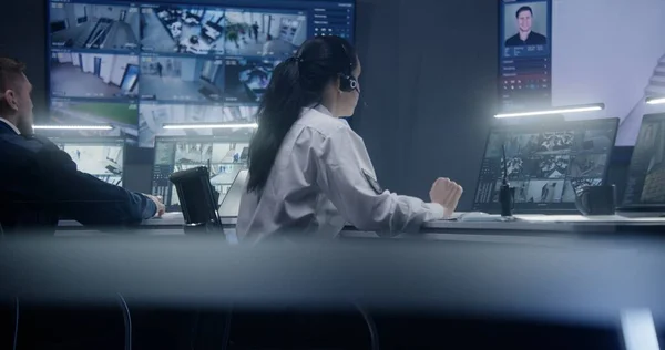 女操作员在警察监视室内用人工智能面部识别键盘和监控摄像头 电脑显示器和墙上有显示闭路电视摄像头的大数字屏幕 — 图库照片