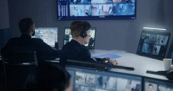 Female security officer watches security cameras with AI facial recognition with male colleagues. Monitoring center workers. Computer monitors and big digital screens with CCTV cameras video footage.