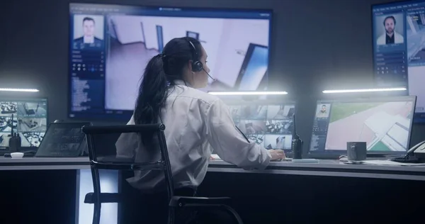 女操作员在警察监视室内用人工智能面部识别键盘和监控摄像头 电脑显示器和墙上有显示闭路电视摄像头的大数字屏幕 — 图库照片