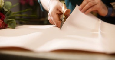 Profesyonel bir çiçekçi masa örtüsü kağıdı koyar ve makasla keser. Çiçekçide çalışma süreci. Yakınlarda güzel bir buket var. Perakende satış işi ve girişimcilik kavramı.