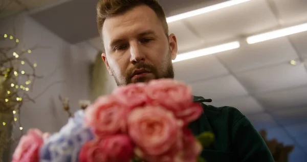 stock image Close up shot of experienced florist working in flower shop. Concentrated man collects beautiful bouquet uses fresh flowers to sale or delivery. Concept of retail floral business and entrepreneurship.