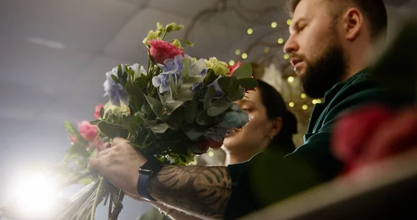 Two entrepreneurs florists together create beautiful bouquet in flowers shop. Man adds fresh flowers to bunch. Woman looks on flower arrangement. Retail floral business and entrepreneurship concept.