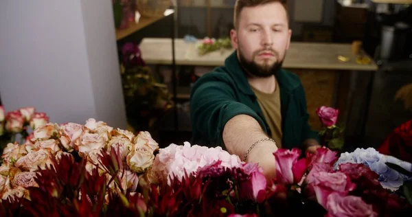 Male professional florist, seller takes fresh beautiful flowers from vase and collects bouquet for customer in flower shop. Concept of floristry, floral retail small business and entrepreneurship.