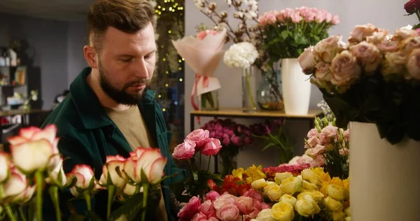 Male professional florist, entrepreneur, seller takes fresh flowers from vase and collects bouquet for client in flower store. Concept of floristry, floral retail small business and entrepreneurship.