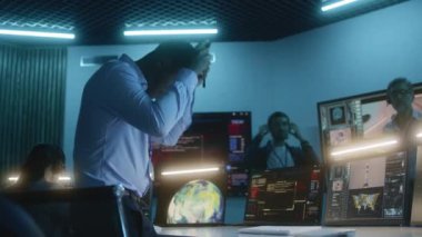 Afro-Amerikan uçuş kontrol çalışanı kulaklığı takıyor, bilgisayarların başına oturuyor, görev kontrol merkezindeki uzay görevini izliyor. Ekip uzay roketinin fırlatılışını arka plandaki büyük dijital ekranlarda izleyin.