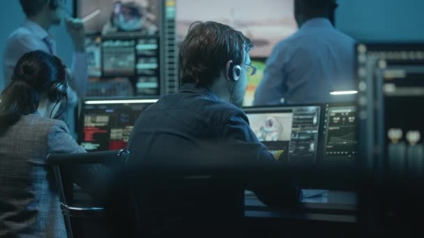 ヘッドセットの男性と女性の飛行制御従業員は コマンドセンターのコンピュータ上のスペースミッションを監視します 大きなデジタル画面に表示された成功した宇宙ロケットリフトオフ後のチームクラップ手 — ストック動画
