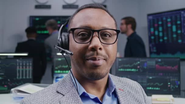 African American Trader Headset Sitter Arbetsplatsen Ler Och Tittar Kameran — Stockvideo