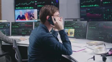Erkek borsacı telefonla konuşuyor. İşadamları komisyoncu bürosunda çalışır. Bilgisayar monitörleri, gerçek zamanlı hisse senetleri, borsa grafikleri ve televizyon haberleri olan büyük ekranlar. Yatırım, ticaret ve analitik.