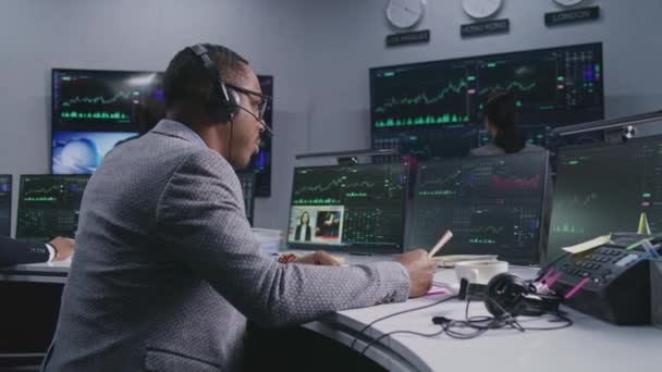 手握钢笔的非裔美国商人在电脑上工作 拥有实时股票 同事们在大屏风的背景下分析外汇市场图表 贸易和投资的概念 — 图库视频影像