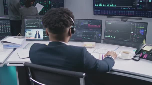 ヘッドセットのアフリカ系アメリカ人金融アナリストは オフィスにリアルタイム株式を持つマルチモニターPc上で動作します チームは大きなデジタル画面に表示される取引所市場チャートを分析します — ストック動画