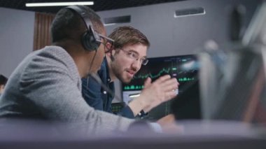 Karışık yarış borsacıları konuşur ve bilgisayardaki gerçek zamanlı hisse senedi verilerini izlerler. İş arkadaşları komisyoncu bürosunda çalışır. Döviz piyasası grafiklerini gösteren büyük dijital ekran. Yatırım ve analiz.