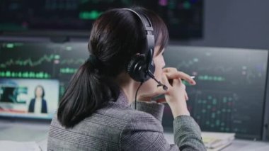 Bankada çalışan kulaklıklı kadın finansal analistin yakın çekimi. Gerçek zamanlı hisse senetleri, borsa grafikleri, grafikleri ve televizyon haberleri olan çoklu monitörlü bilgisayar. Analizler, kripto para ticareti