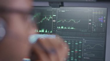 Komisyoncu ofisinde çalışan kulaklıklı Afro-Amerikan borsacının yakın çekimi. İşadamı bilgisayar ekranına bakıyor, gerçek zamanlı hisse senetlerini izliyor, borsa grafiklerini değiştiriyor. Kripto para ticareti.