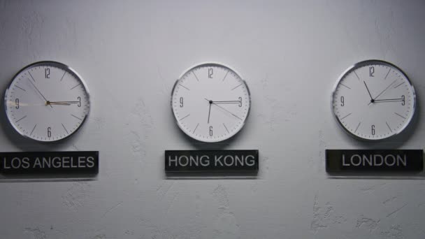 用现代设计在办公室里静止不动地拍摄墙上的时钟 带有运行时间指针的白色手表显示了不同城市的时区 在时钟下书写的大城市的名称 时间流逝 — 图库视频影像