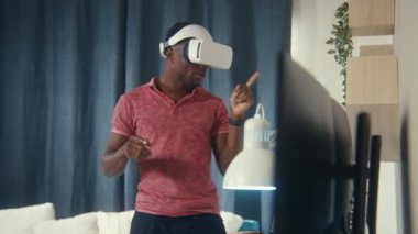 Afro-Amerikalı erkek duygusal konuşmaları ve sanal gerçeklik kulaklığı kullanarak online konferansta el kol hareketleri. Oyuncu evdeki artırılmış gerçeklik oyununda oynuyor. İş ve günlük hayatta yüksek teknoloji araçları kullanma kavramı