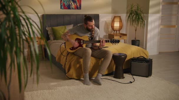 男性音楽家は寝室でギターを演奏する ドラムセットとウクレレを演奏し 隣に住んでいる若い男の子と女の子にカメラのパン 壁で区切られた2つの部屋やアパートのビュー 近所の概念 — ストック動画