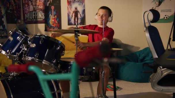 戴耳机的小男孩在家里用鼓包练习音乐技巧 照相机改变了人们对老邻居唱歌和弹奏电吉他的看法 被墙隔开的公寓 鞭子盘 — 图库视频影像